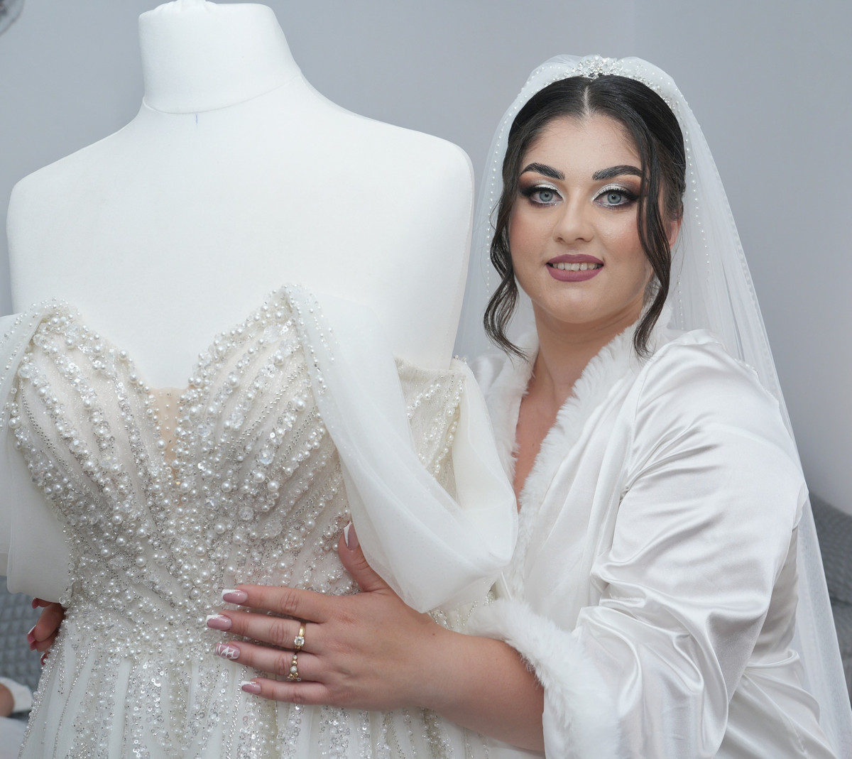 Mireasa în halat, lângă rochia de mireasă așezată pe manechin